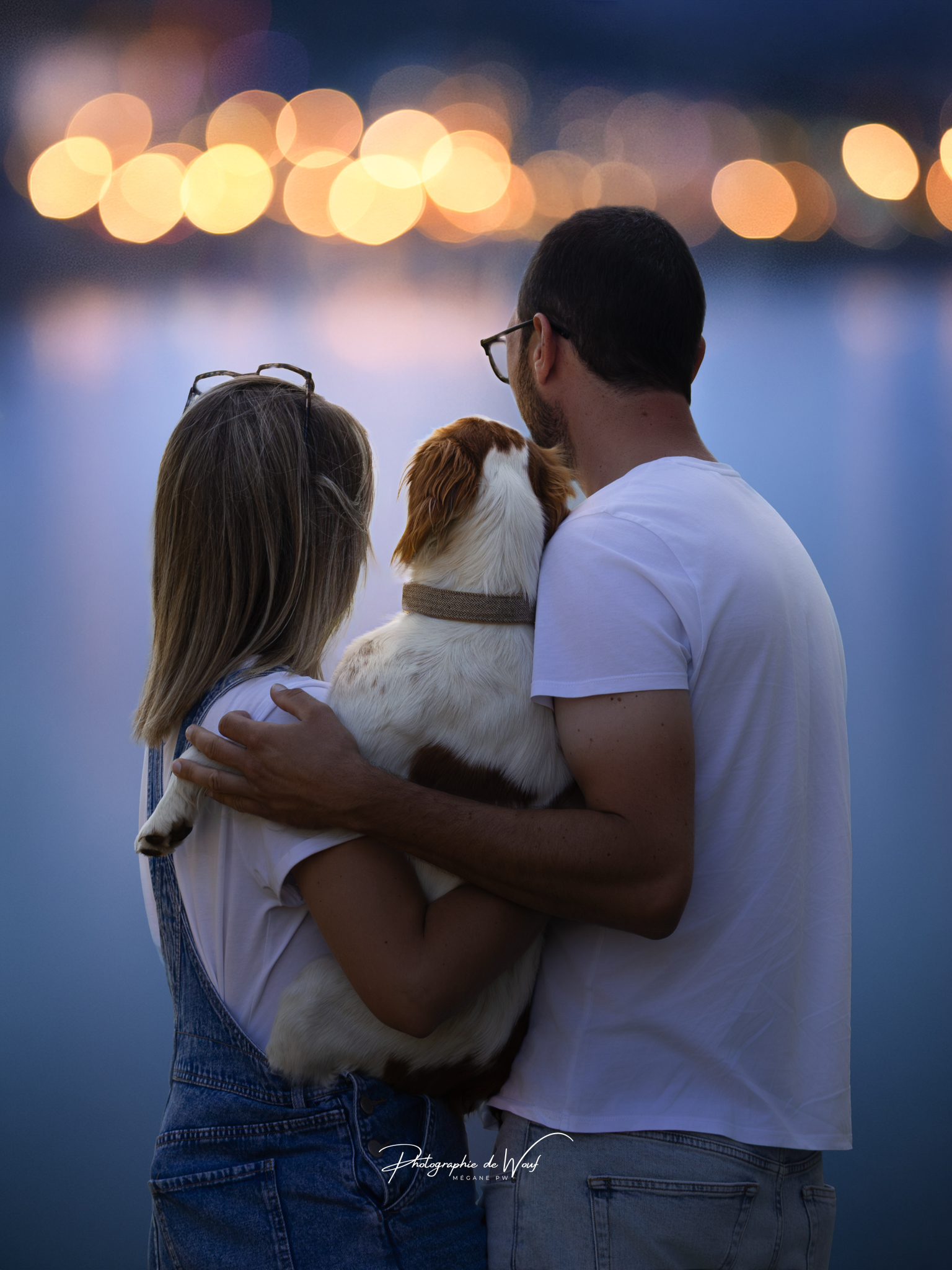 Photographie d'un couple et leur chien Epagneul breton, la nuit, face à un bokeh de lumière